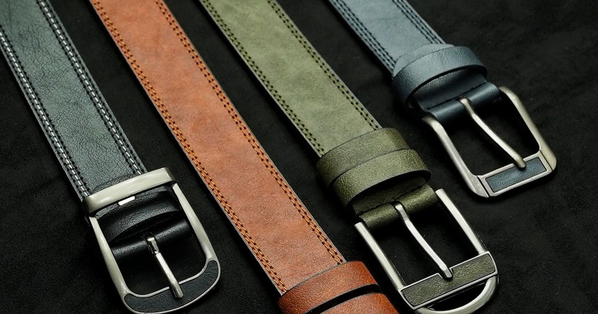 A collection of four stylish leather belts in various colors lying on a black surface.