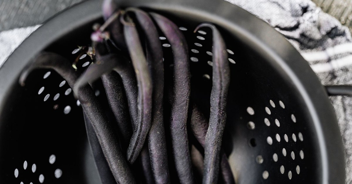 Fresh purple string beans in a black colander, ready for cooking.