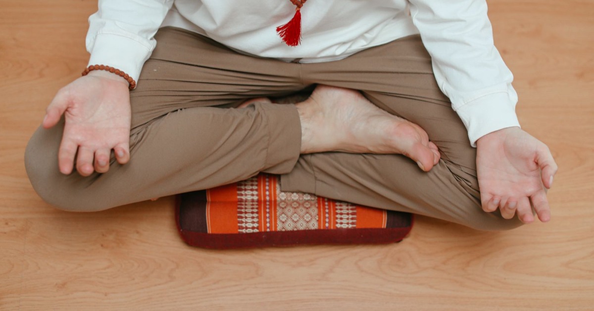 Overhead view of a man meditating at home, sitting in a yoga pose on a wooden floor.
