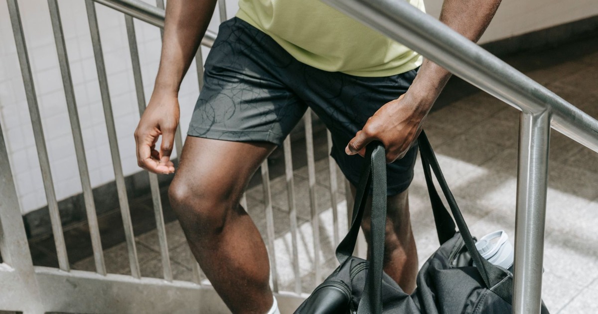 Man in athletic wear carrying a gym bag up a stairway, emphasizing fitness lifestyle.