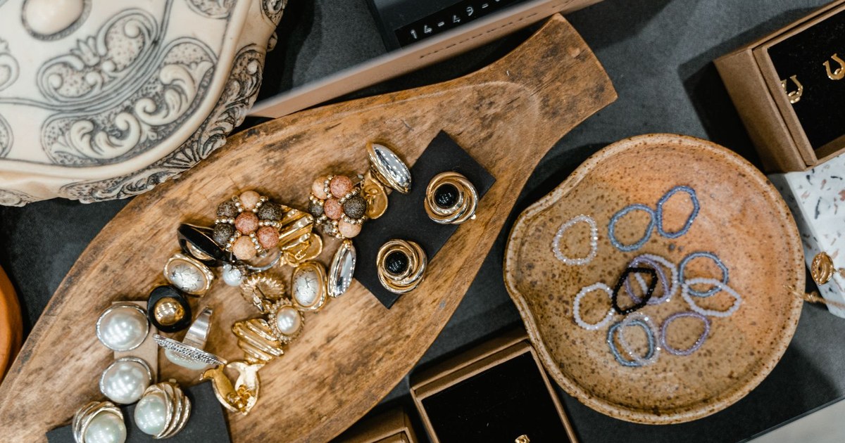 A top view of assorted jewelry including rings and bracelets in a wooden tray and ceramic dish.