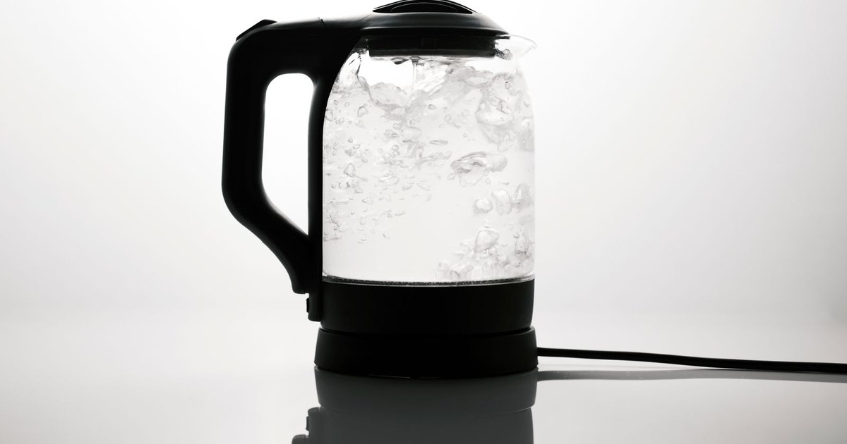 A sleek electric kettle boiling water, captured on a reflective white surface.