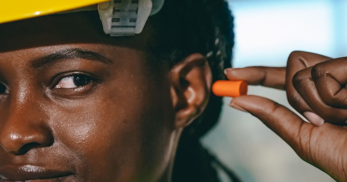 Close-up of a woman wearing a hard hat and fitting earplugs for safety on site.