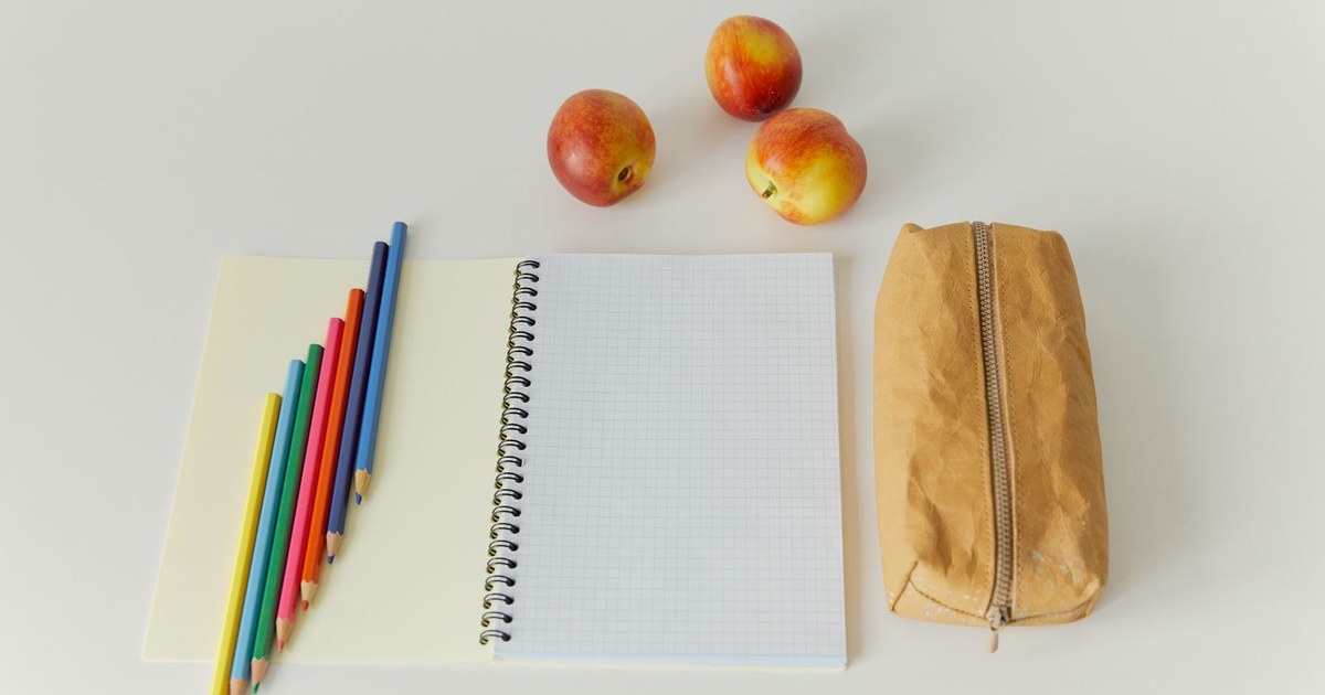 Artistic workspace with colored pencils, apples, and a notebook on a table.