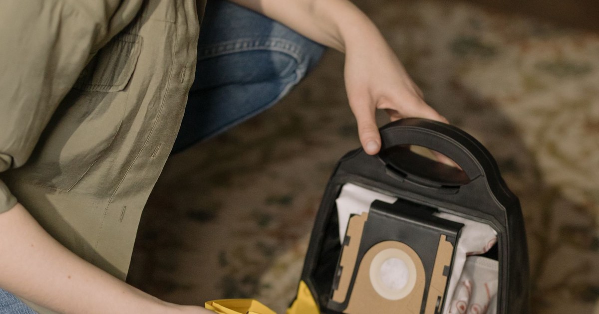 A woman changes the vacuum cleaner bag while cleaning at home, focusing on household maintenance.