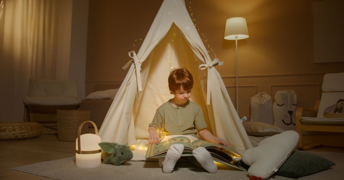 Young boy reading a book in a cozy tent with warm lighting indoors, perfect for storytelling.