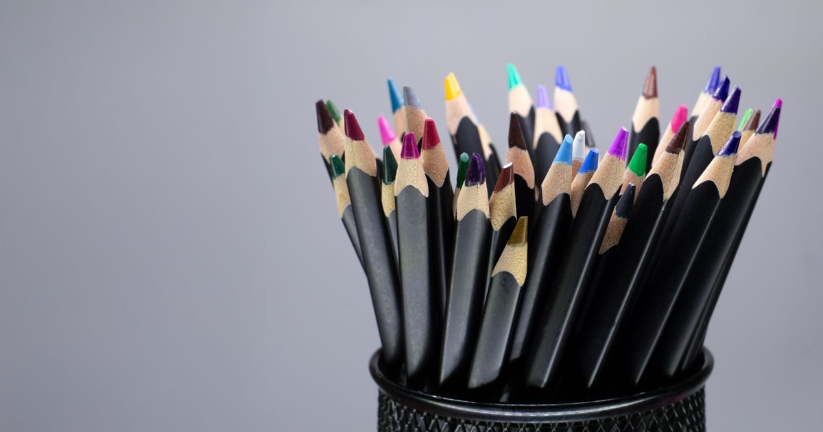 A collection of colorful pencils in a black mesh holder against a gray background.