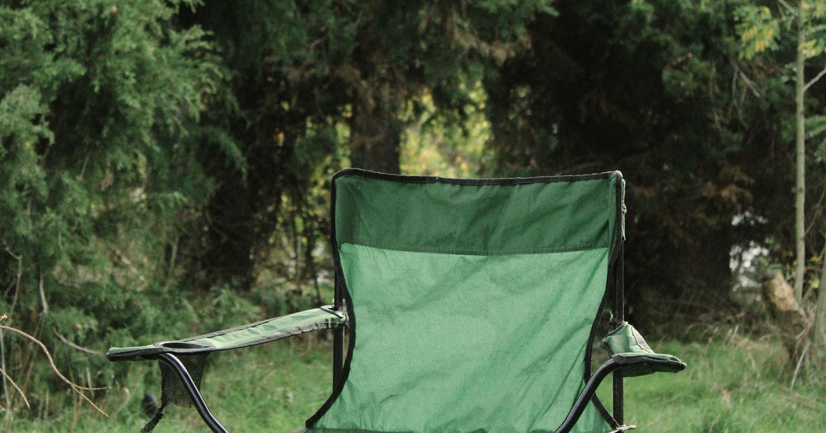 A green folding camping chair sits in a verdant forest clearing, evoking tranquility.