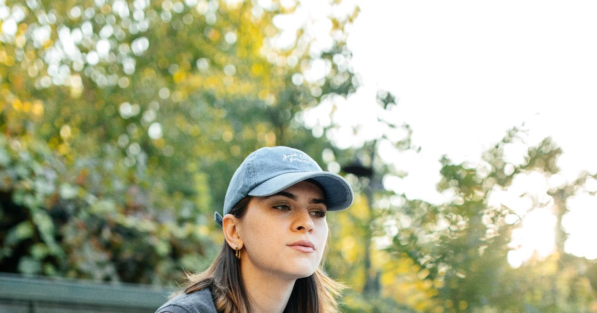 Young woman wearing casual clothing sitting on a car outdoors during the day.