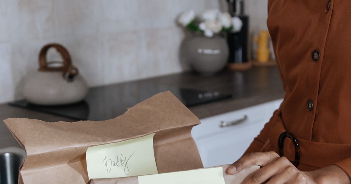 Parent preparing labelled lunch bags for children in a kitchen