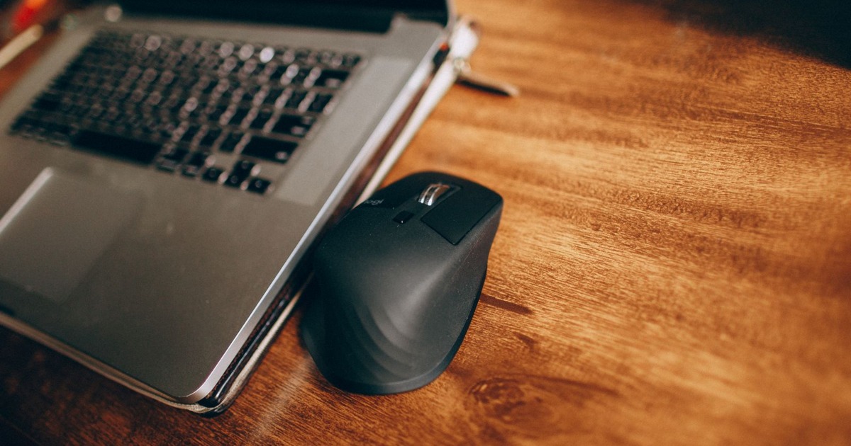 A wireless mouse and laptop placed on a polished wooden desk, perfect for office and remote work setup.