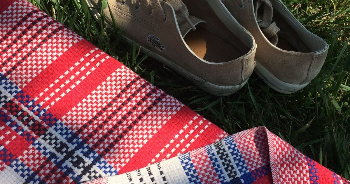 A casual outdoor picnic scene featuring shoes and a colorful blanket on green grass.