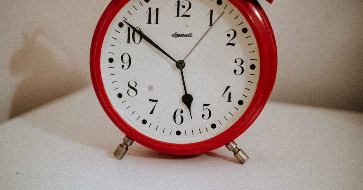 Vintage red alarm clock with white face and black numerals on a white surface.