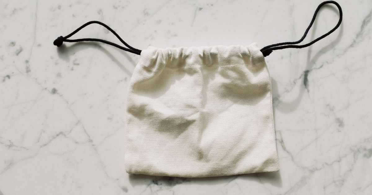A simple white drawstring pouch on a marble surface, perfect for storing small items.