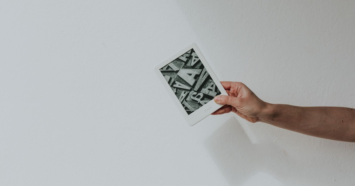 A minimalist photo of a hand holding a modern e-reader against a white background.