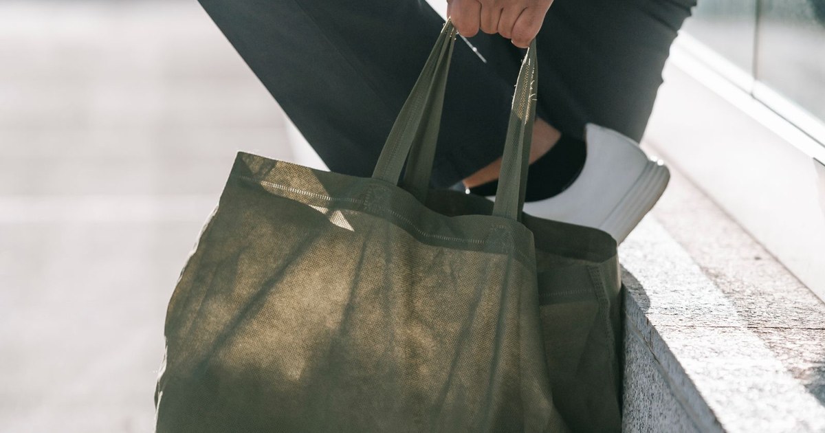Side view of crop anonymous male in trendy clothes with natural bag and raised leg standing on urban pavement