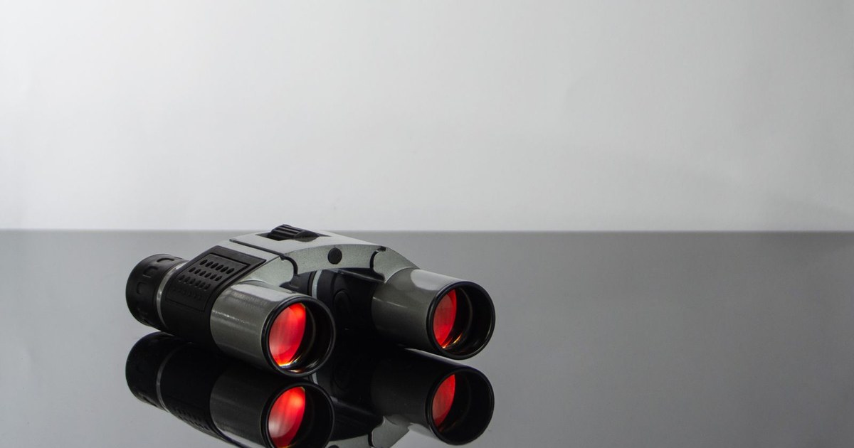 Close-up of modern binoculars with red lenses reflecting on a sleek glass surface.