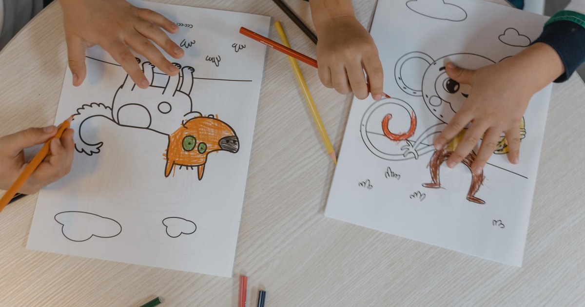 Children using colored pencils to bring animal drawings to life on a wooden table.