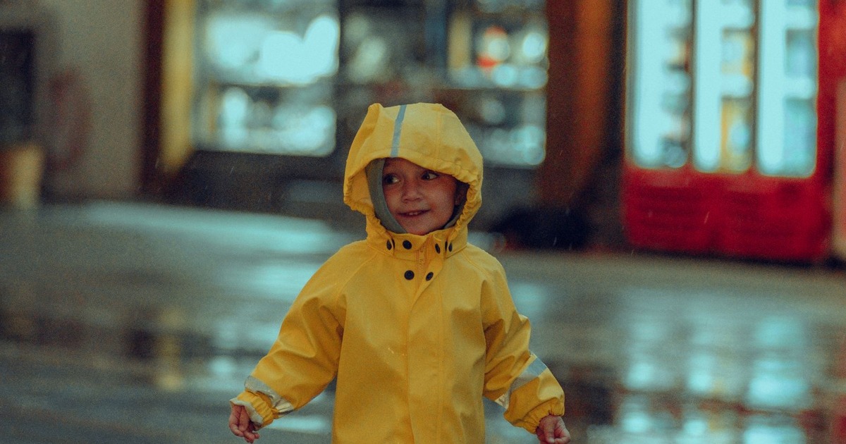 Adorable child wearing a yellow raincoat and boots, enjoying a rainy evening outside.