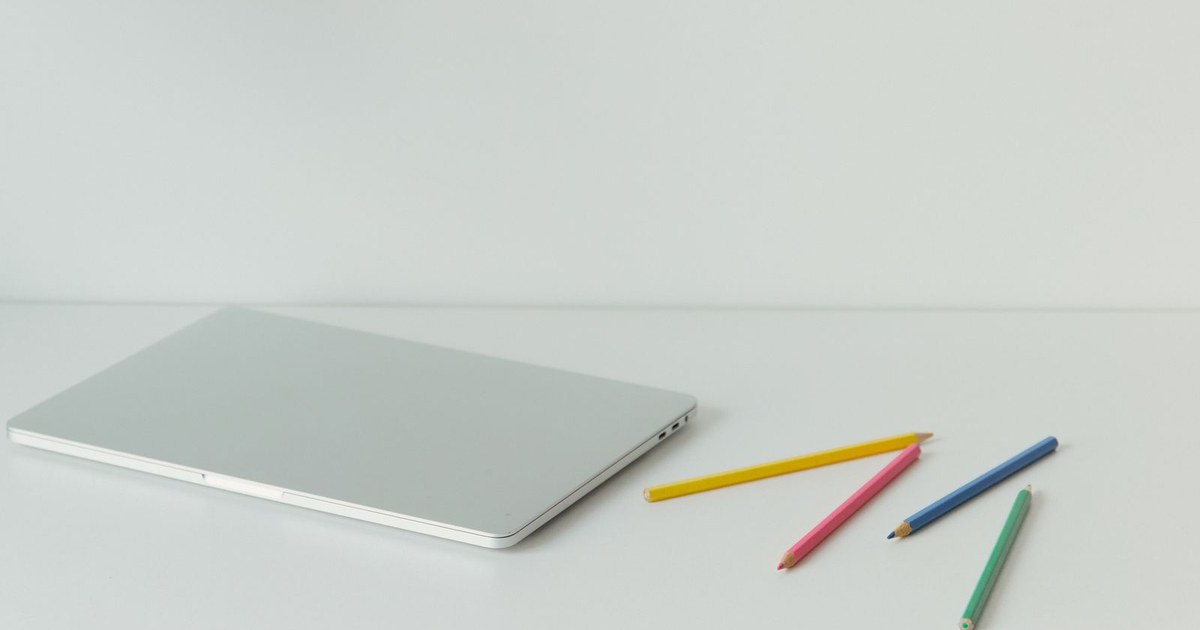 A minimalist home office desk with a laptop and colored pencils on a white surface.