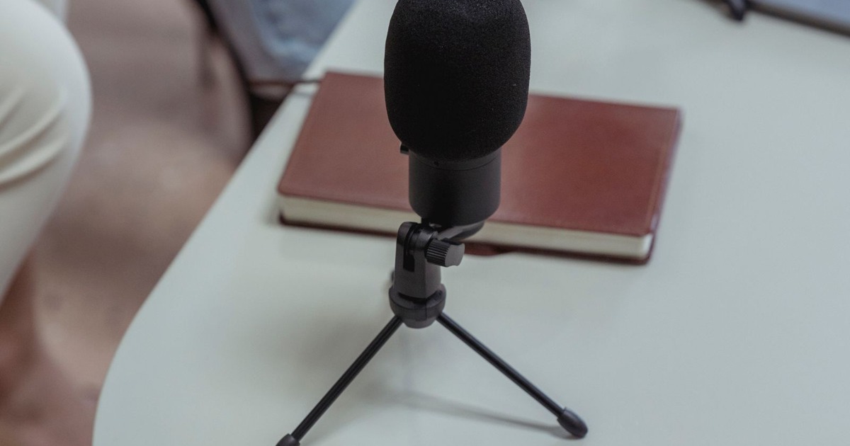 Close-up of microphones, a notebook, and laptops on a white table, ideal for podcasting.