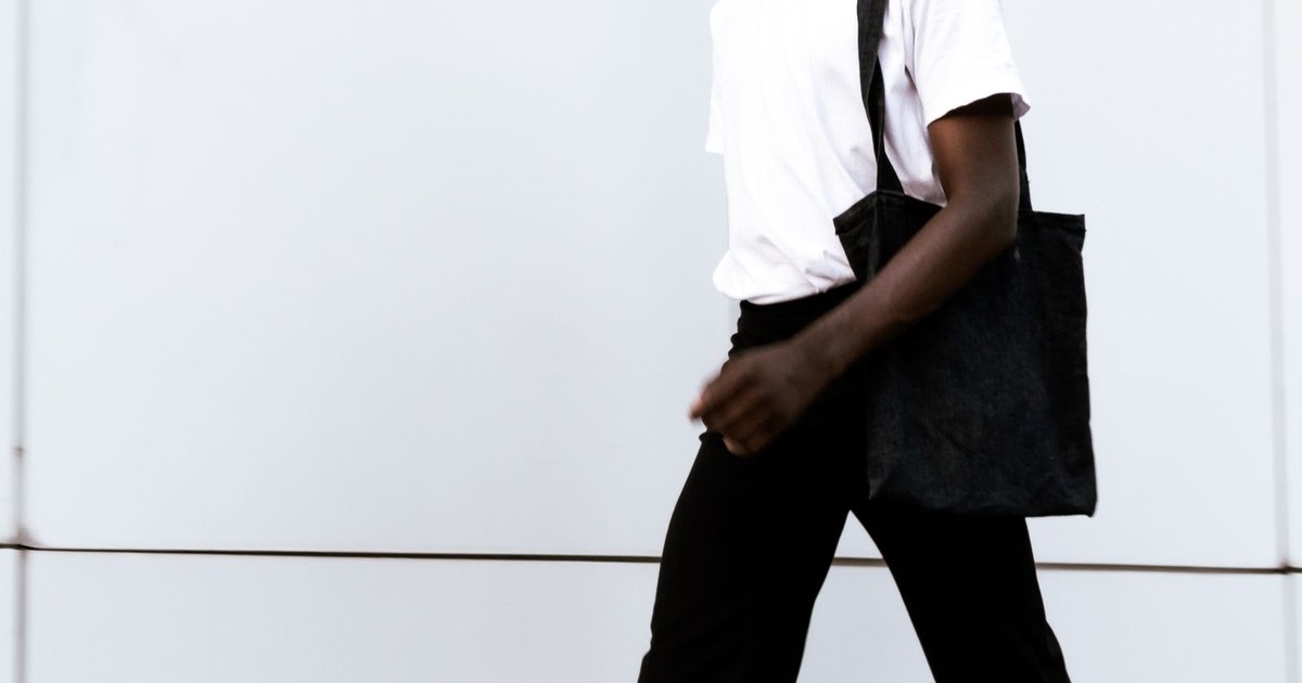 Fashionable adult walking with tote bag in urban setting, showcasing casual style.