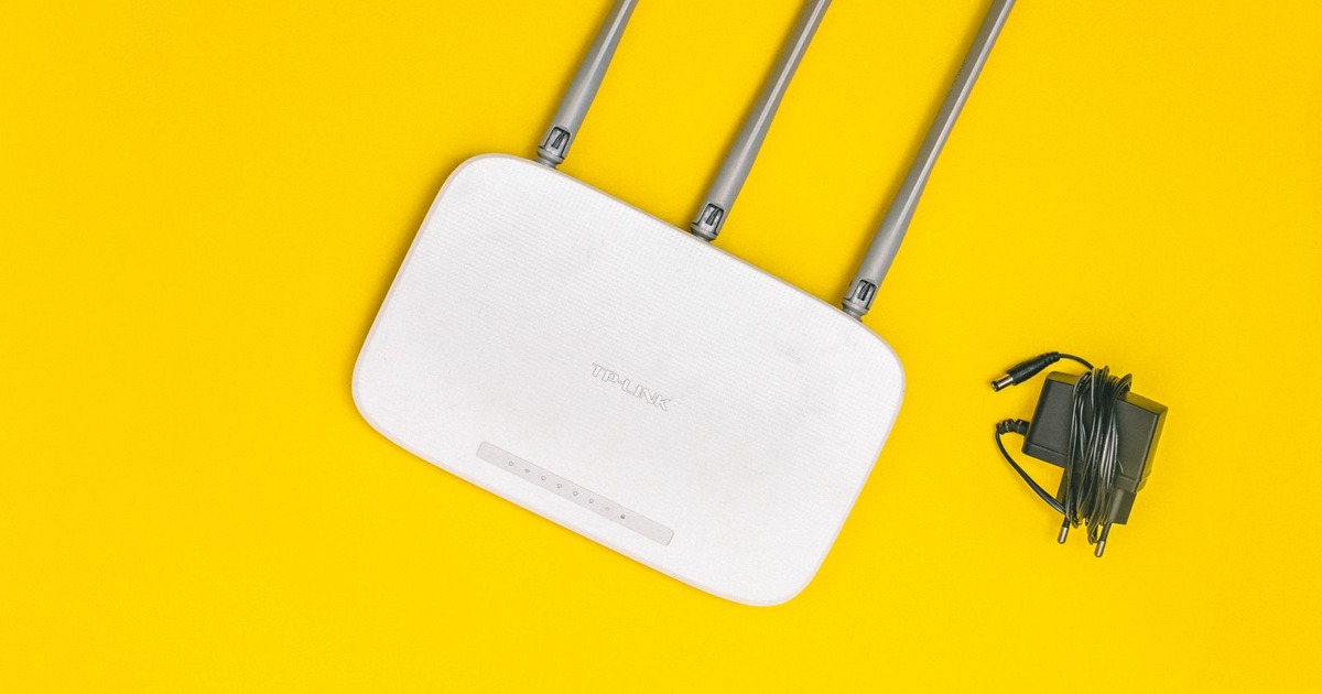 White router with three antennas and cables on bold yellow background, ideal for tech concepts.