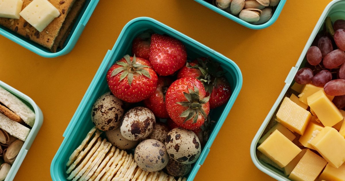 Top view of diverse snacks in bento boxes on yellow background.