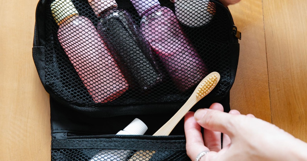 Open toiletry bag with bottles and a bamboo toothbrush on wooden surface.