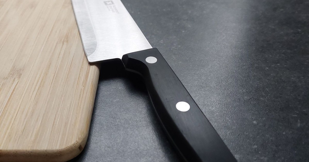A sharp kitchen knife resting on a wooden cutting board on a dark countertop.