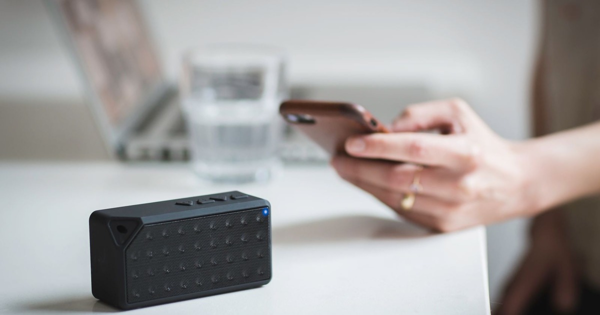 Person connecting a smartphone to a wireless speaker indoors, foreground focus.