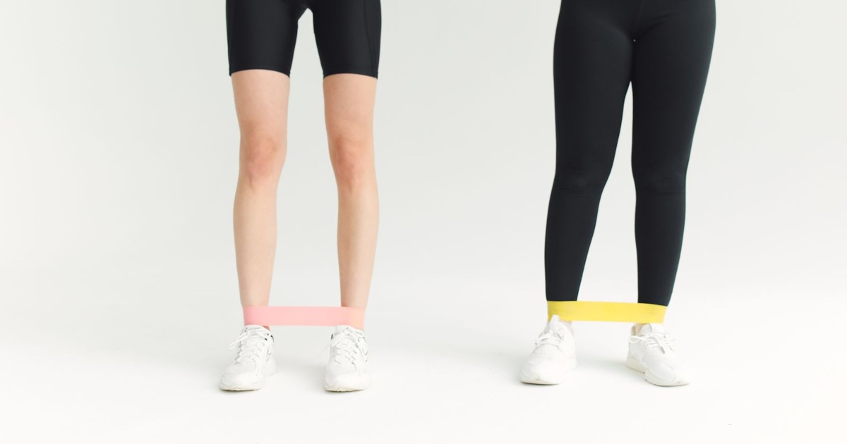 Two women in activewear using resistance bands during an indoor workout session.