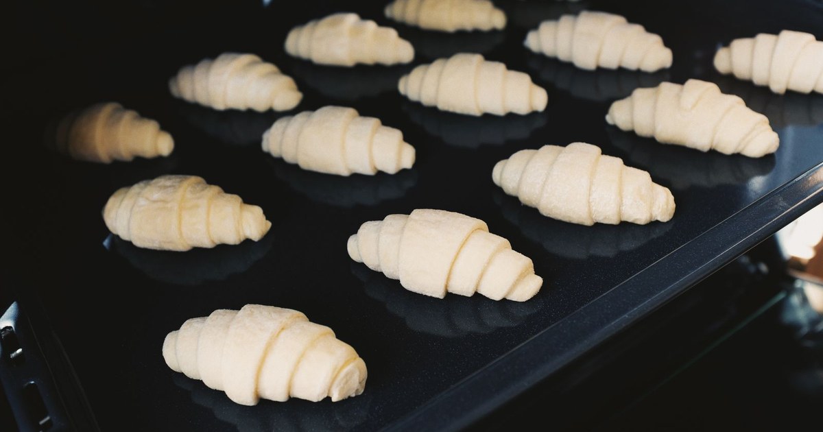 Close-up of uncooked croissants on a baking tray in an oven, captured indoors.