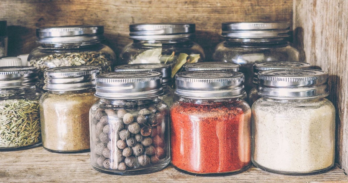 A collection of assorted spices in glass jars on a rustic wooden shelf for culinary use.