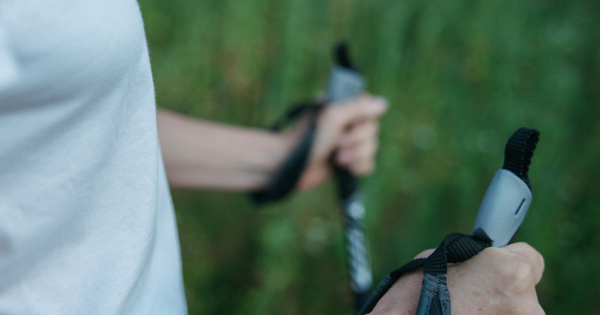 Close-up of a woman holding trekking poles, surrounded by lush greenery, outdoors.