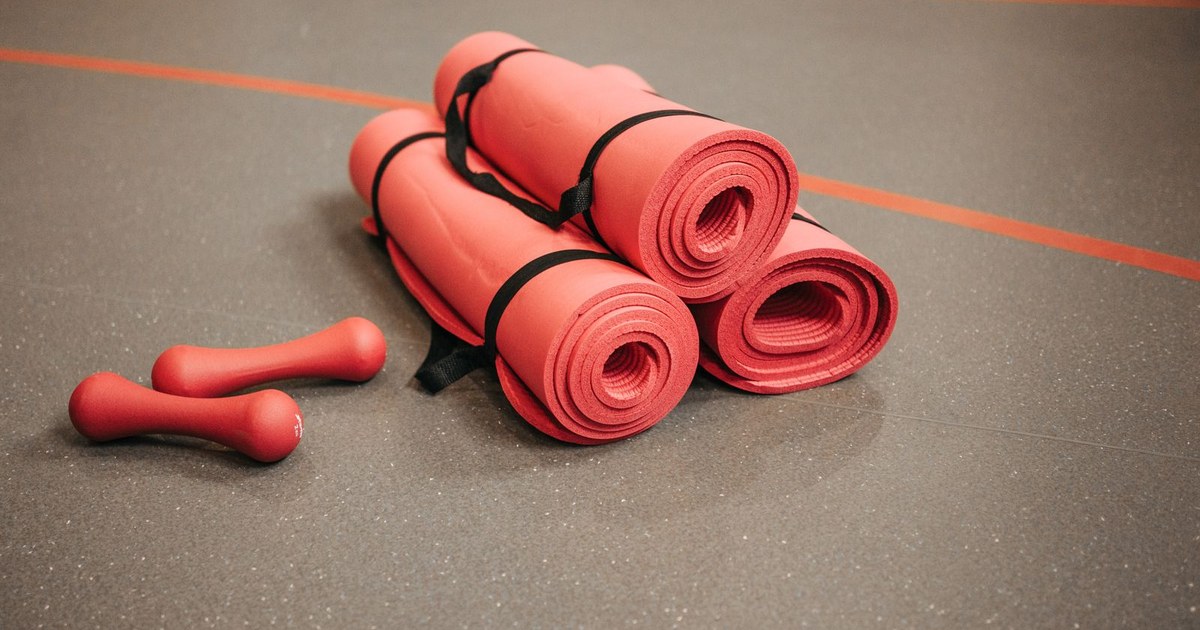 Red exercise mats and dumbbells on a gym floor, perfect for home or studio fitness.